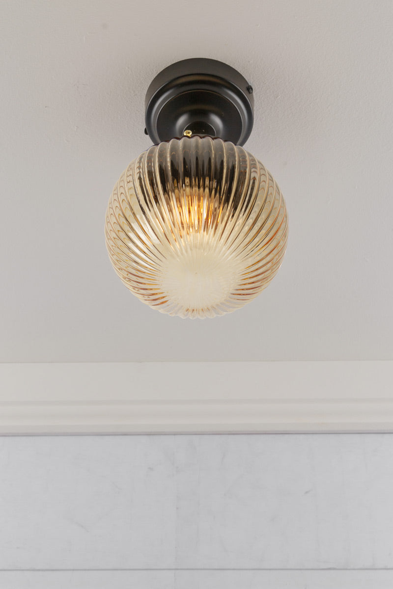 Under view of an amber reeded glass ball shade on a black flush mount that is IP rated. 