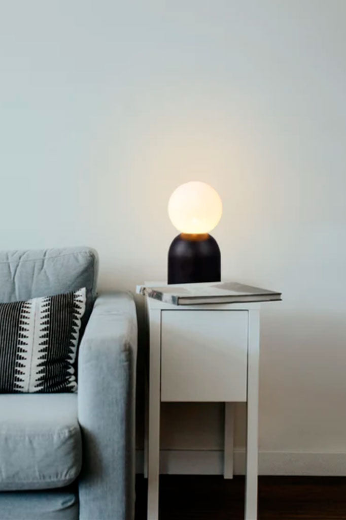 Black lamp illuminating a coffee table next to a sofa.