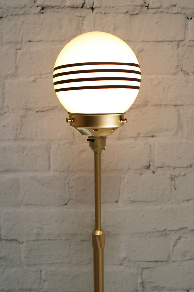 Close up of a small opal glass ball shades with four stipes on a gold/brass lamp stand