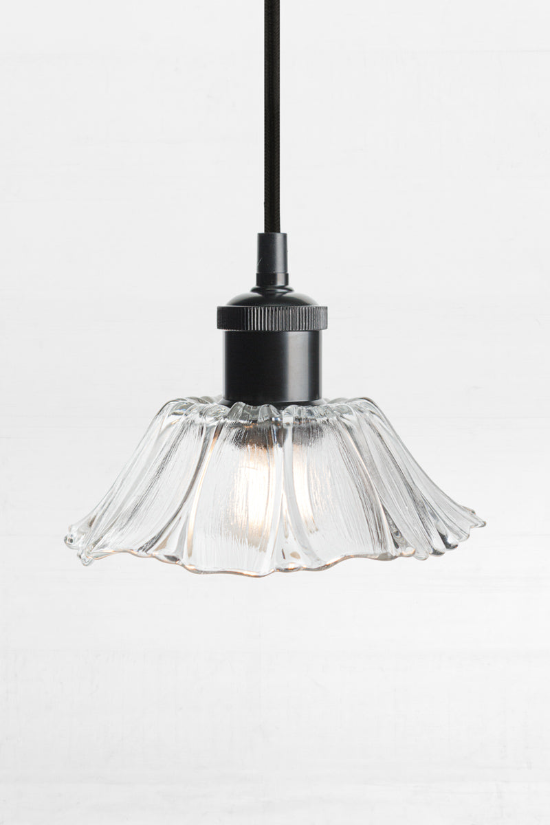 Floral shaped clear glass on black lampholder with black cord. 