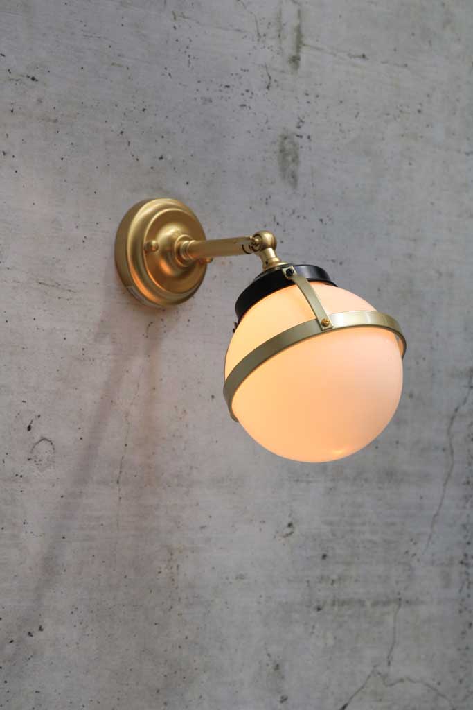 Huxley wall light with long gold arm and small opal shade in tilted position