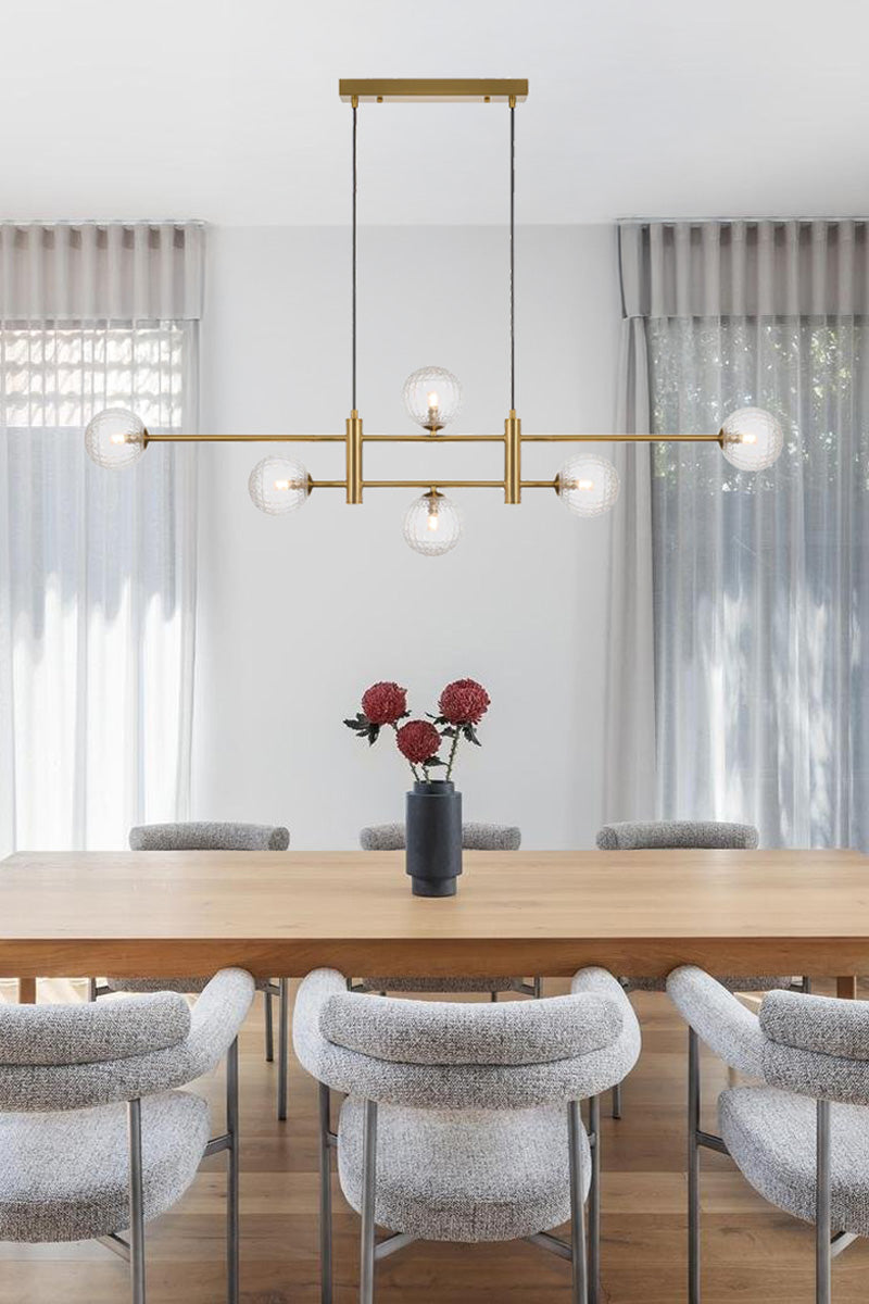 Gold 6 light linear chandelier with glass ball shades in a clear prism finish, hanging above a dining space.  