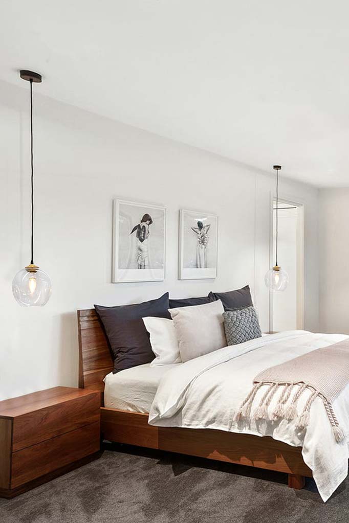 Two clear glass spherical shades hanging from black cords in a bedroom. 