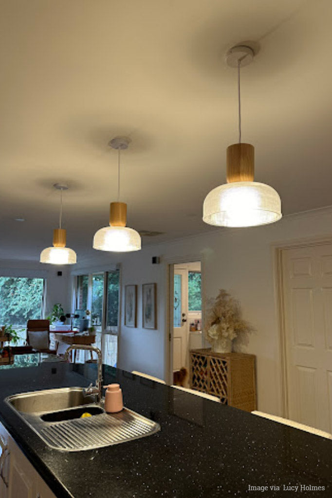 Image via Lucy Holmes, 3 Chapman large shades with nord wood blocks hanging over a kitchen bench.