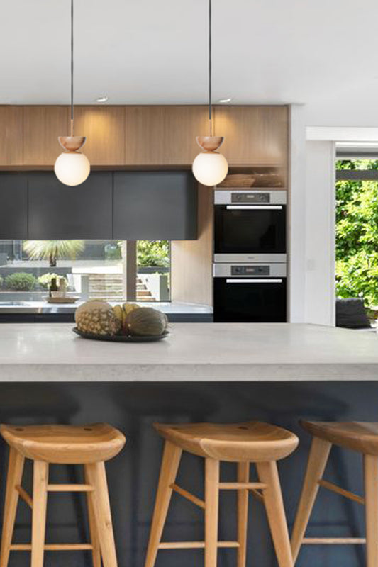 Two opal glass ball pendant lights with half circle wood top detailing in a kitchen. 