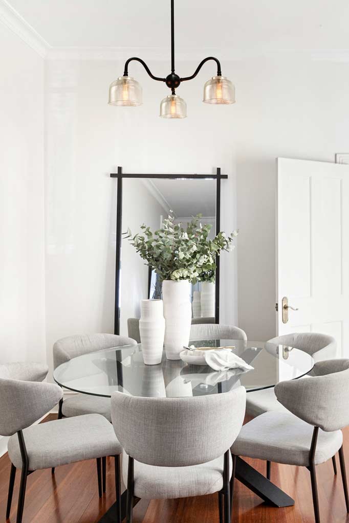 Black three arm gooseneck steel chandelier with clear shades over a dining table.