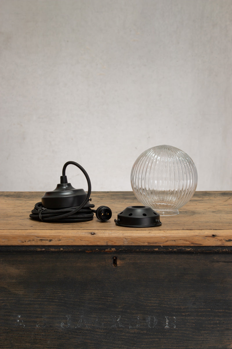 Deconstructed clear reeded glass ball shade on a black pendent cord with black metalware. 