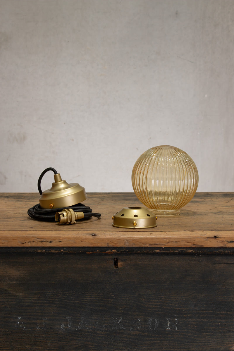 Disassembled Amber reeded glass ball shade on a black pendent cord with gold/brass metalware. 