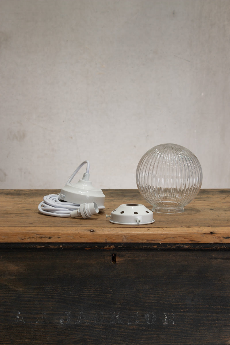 Deconstructed Clear reeded glass ball shade on a white pendent cord with white metalware. 