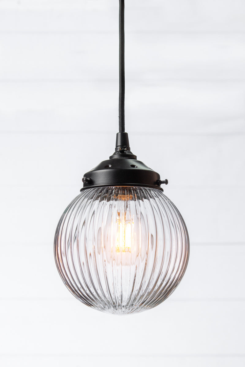 Clear reeded glass ball shade on a black pendent cord with black metalware. 