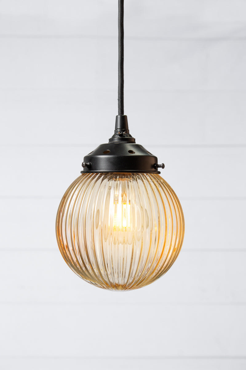 Amber reeded glass ball shade on a black pendent cord with black metalware. 