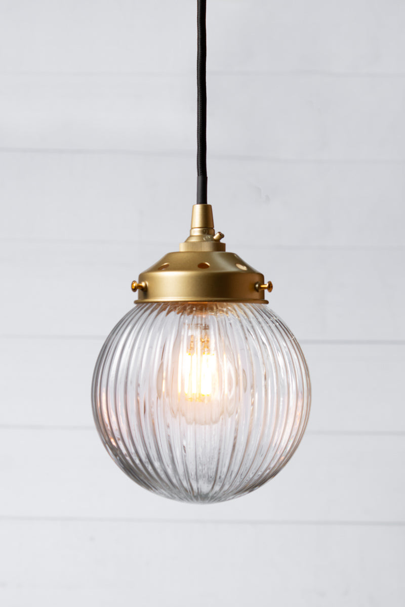 Clear reeded glass ball shade on a black pendent cord with gold/brass metalware. 