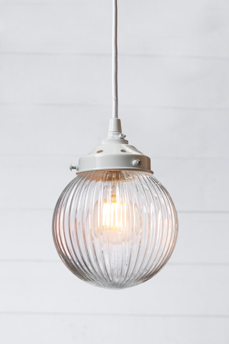 Clear reeded glass ball shade on a white pendent cord with white metalware. 