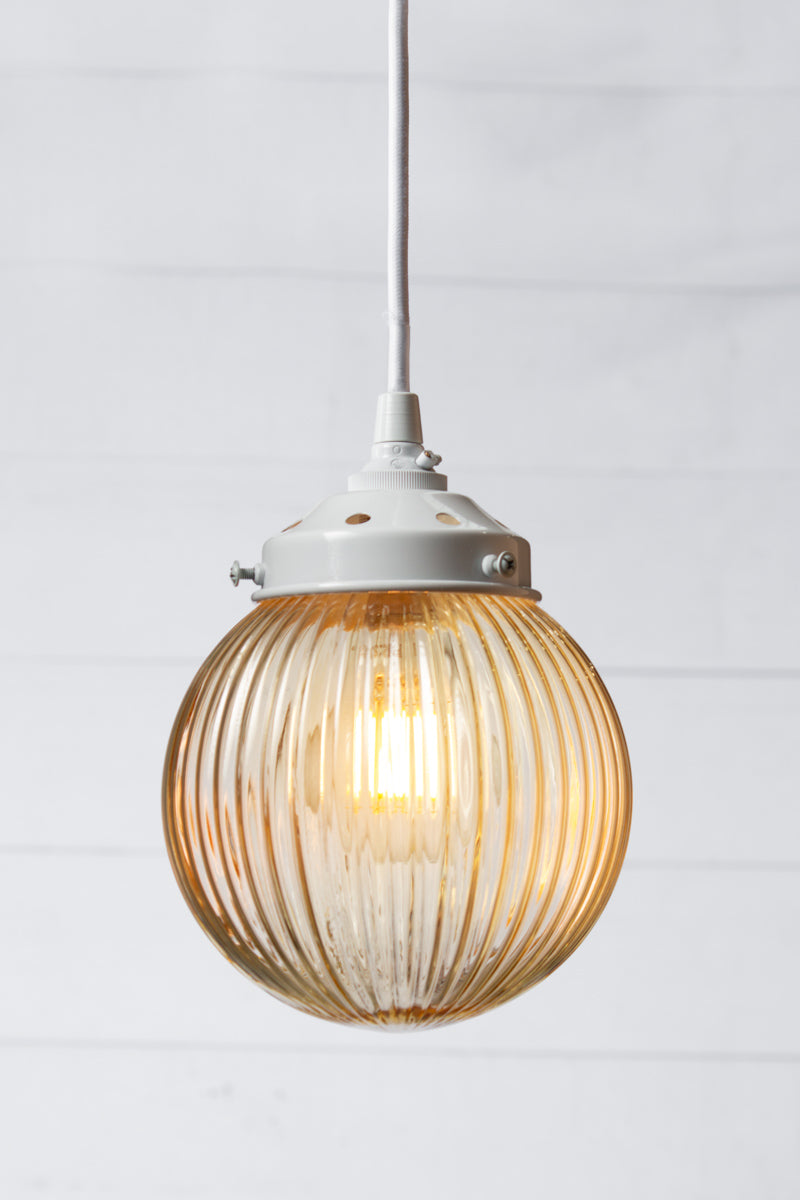 Amber reeded glass ball shade on a white pendent cord with white metalware. 