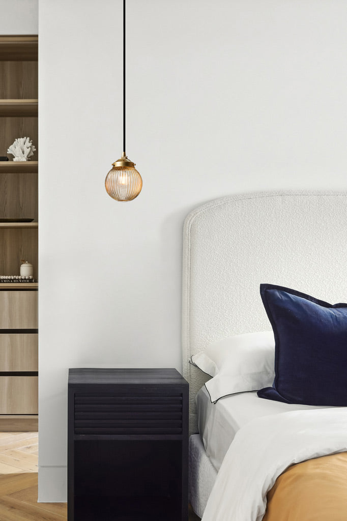 Amber reeded glass ball pendant on a gold/brass gallery and black cord in a bedroom. 