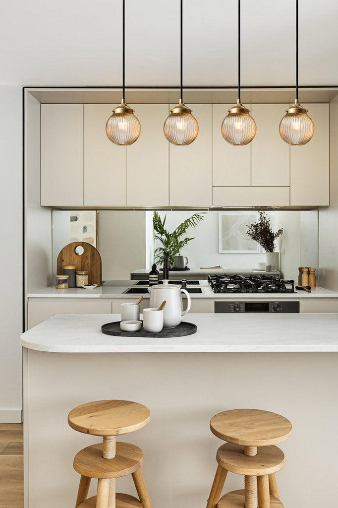 Four amber reeded glass ball pendants on a gold/brass galleries and black cords in a kitchen 