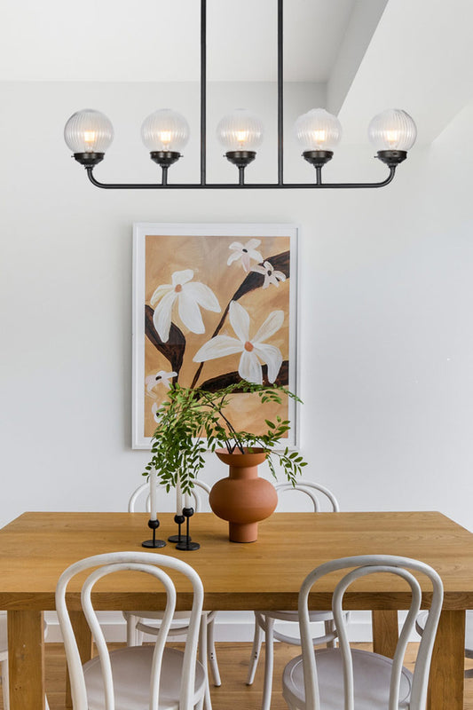 Five light black linear pendant fixture with clear reeded glass shades in a dining space. 