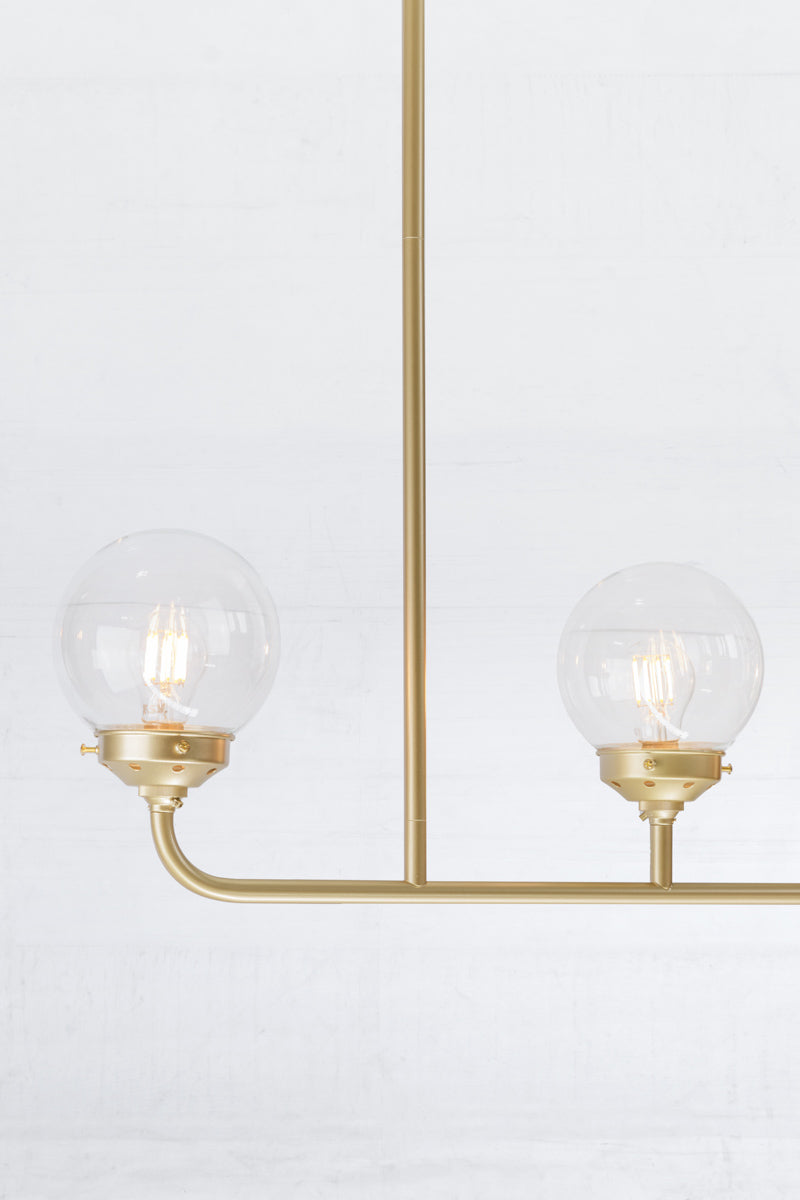 Close up of the  Gold/Brass five lamp linear chandelier with clear glass ball shades.