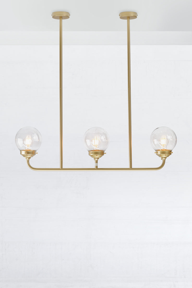 Gold/Brass triple lamp linear chandelier with clear glass ball shades.