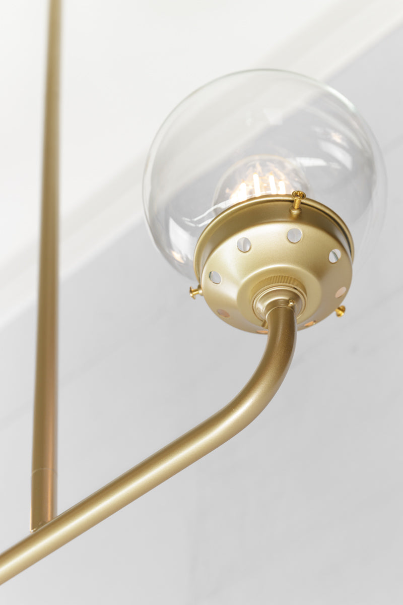 Close up of the Gold/Brass triple lamp linear chandelier with clear glass ball shades.