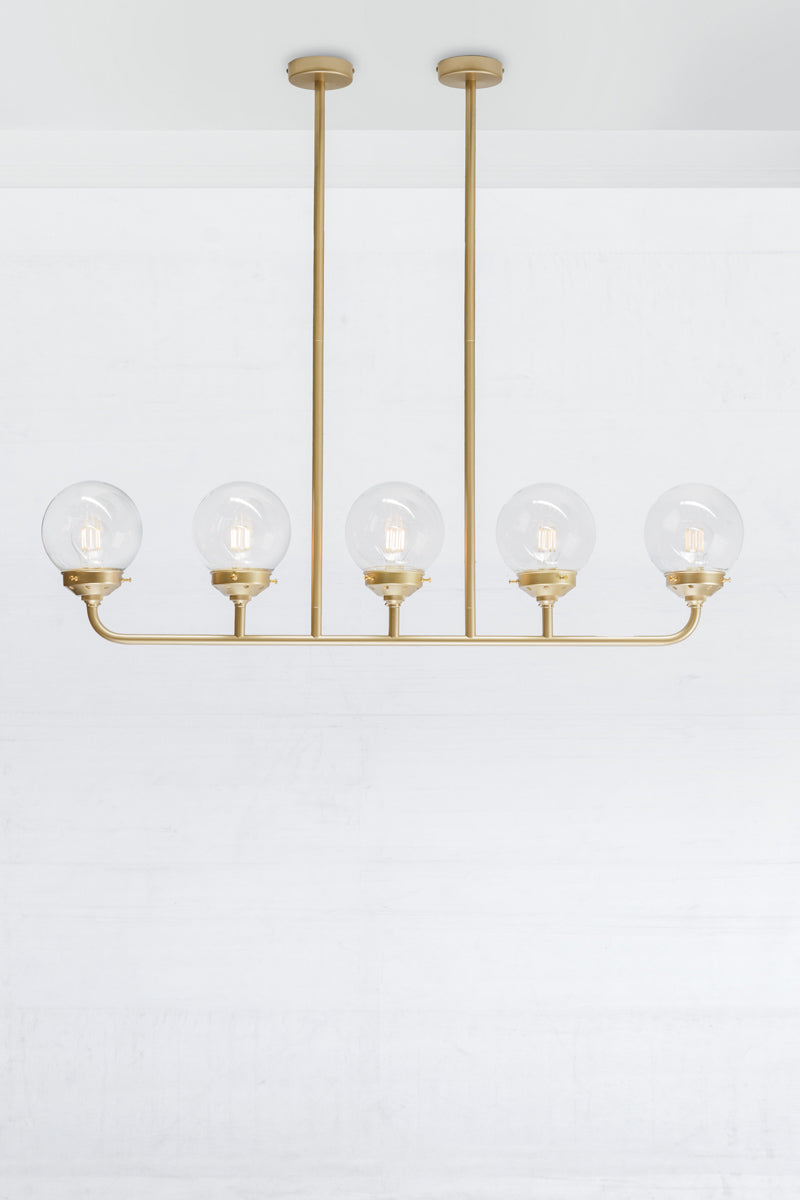 Gold/Brass five lamp linear chandelier with clear glass ball shades.