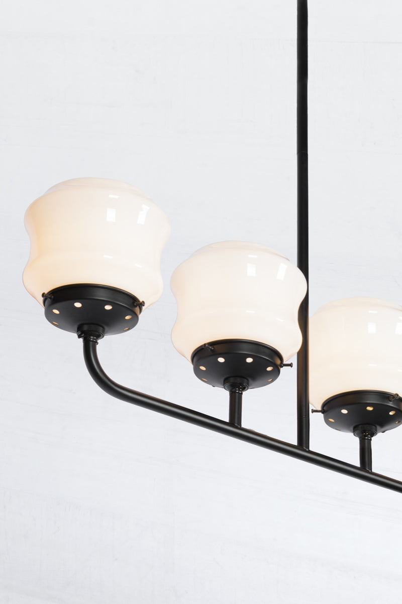 Close up of the Five lamp black linear chandelier with schoolhouse style flinders opal shades. 