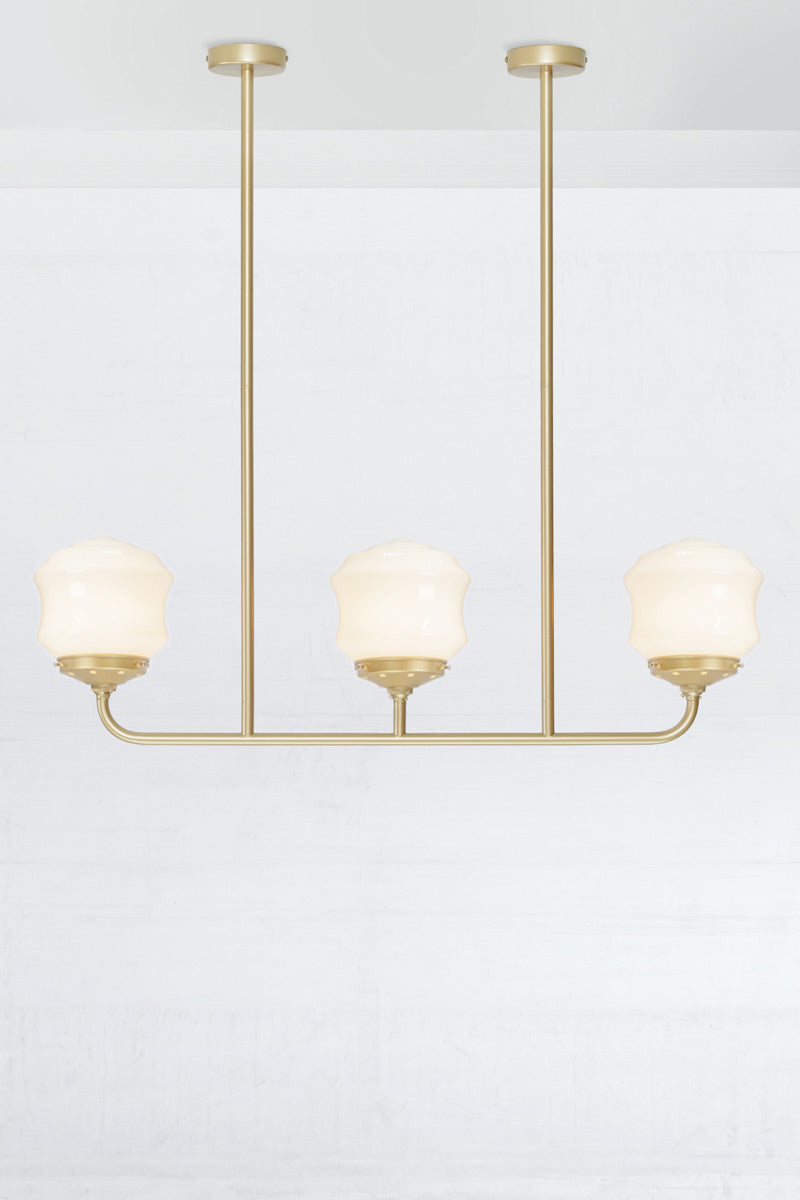 Triple lamp gold/brass linear chandelier with schoolhouse style flinders opal shades. 