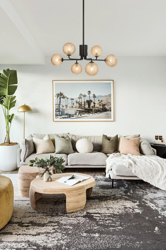 Six arm black chandelier with amber tear glass ball shades in a plush lounge room. 