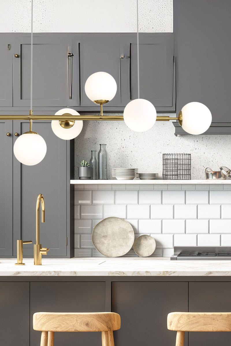 Gold/brass 6 light linear glass ball pendant light in a kitchen.