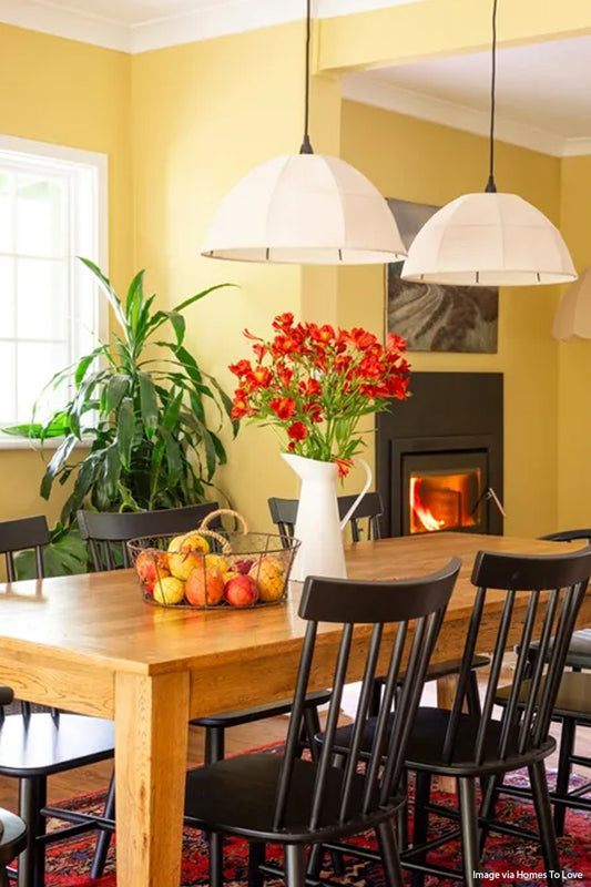 Two farmhouse fabric shades over a bright yellow farmhouse dining space wih red flowers. Image via Homes to Love. 