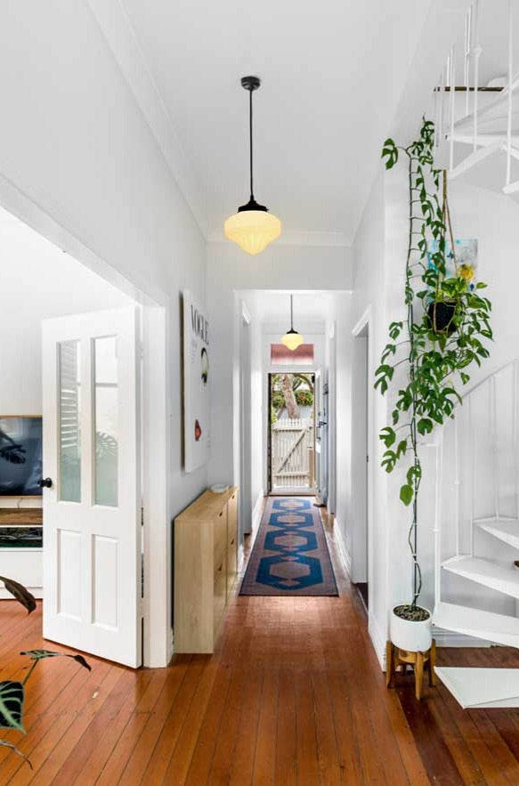  Two opal Auberge schoolhouse pendant light hanging in a white walled entrance hall, with timber floors. 