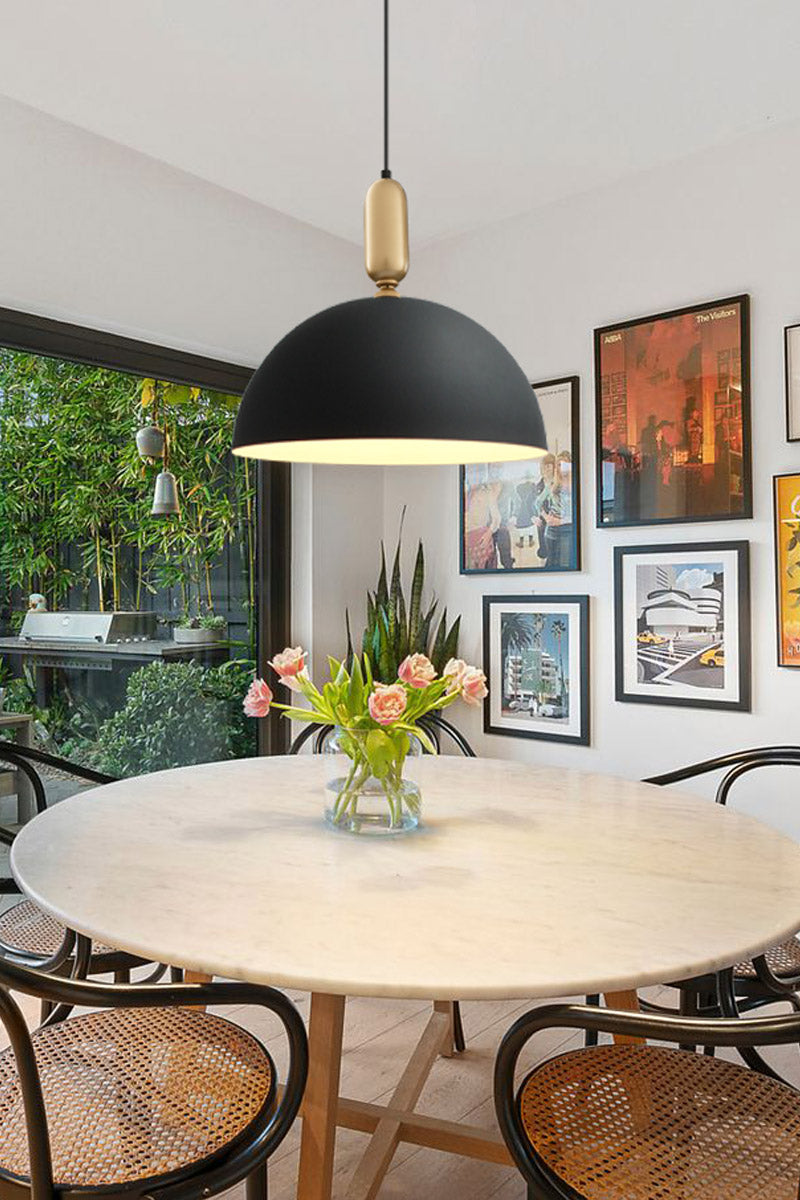 Large black dome shade with gold/brass tube deatil hanging over a dining room. 