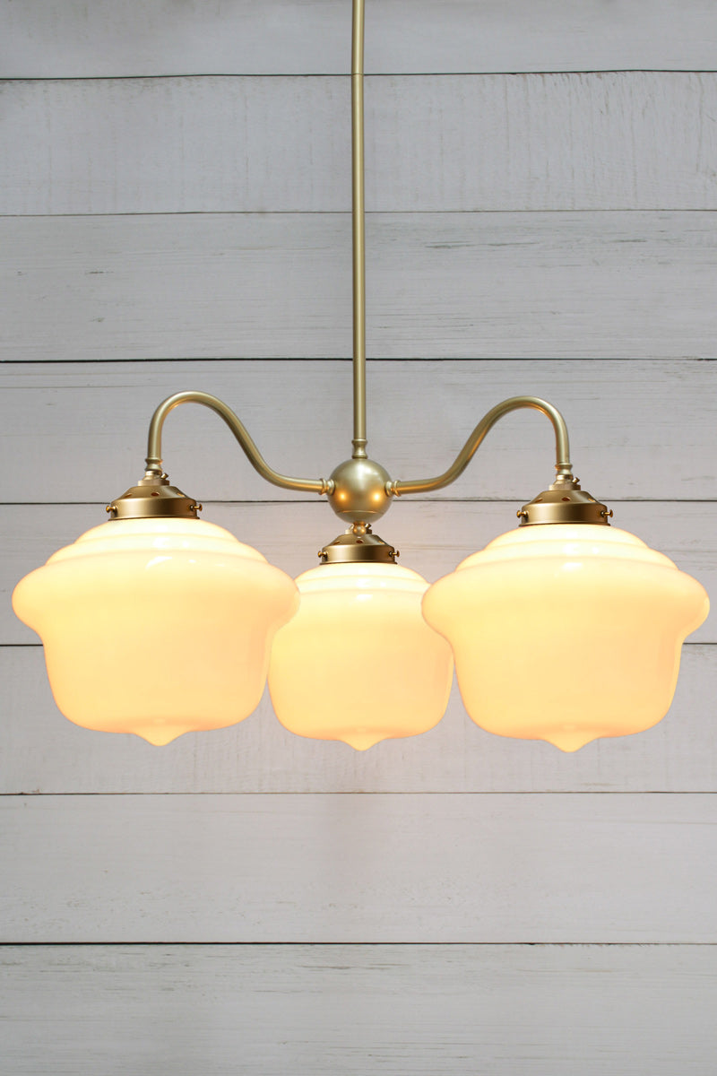 Three schoolhouse shades on a gold/brass gooseneck fixture. 