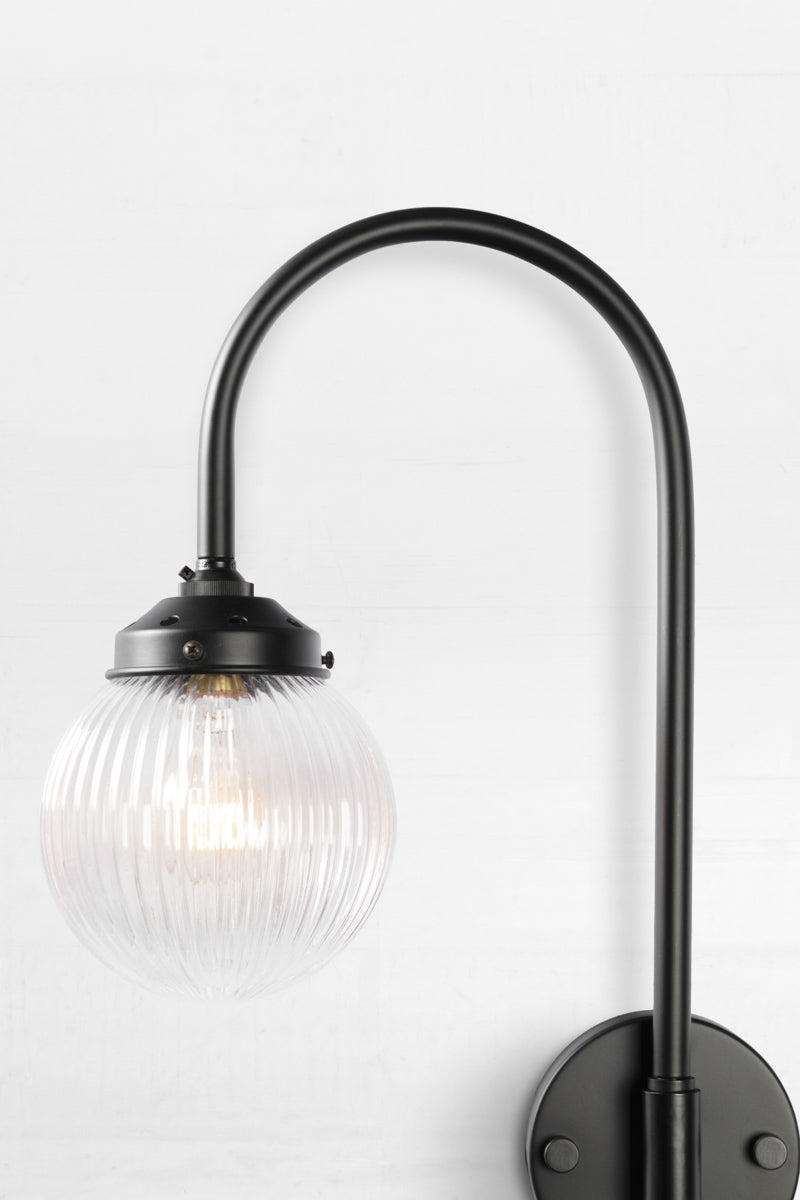 Close up of the Shepard gooseneck wall light in black with a clear reeded glass ball shade. 