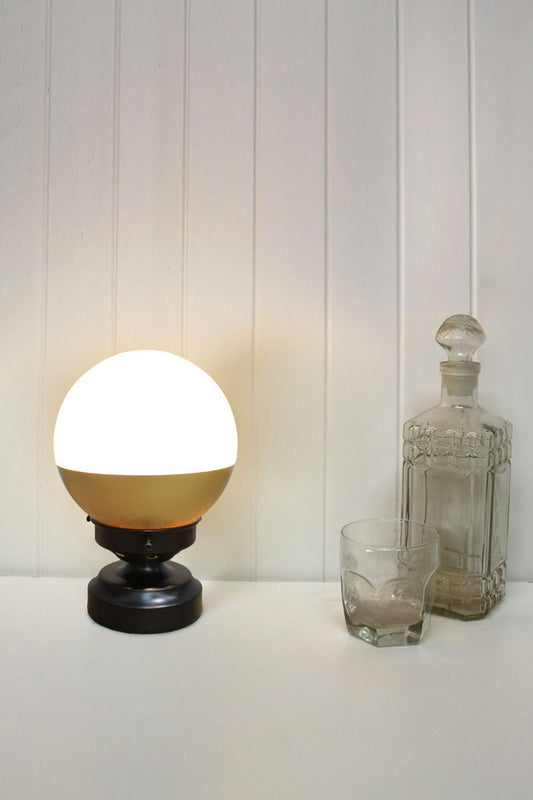 Crown sphere lamp with gold shade and black base on table