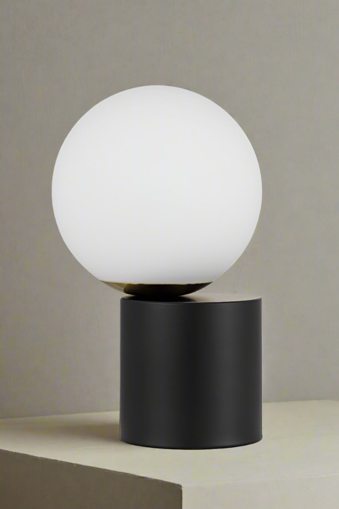 Off centred opal ball shade on a black cylindrical touch lamp base. 