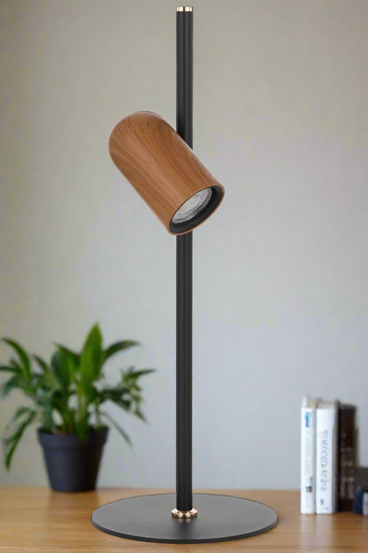 Black table lamp with a painted wood look shade on a table  with a plant and books