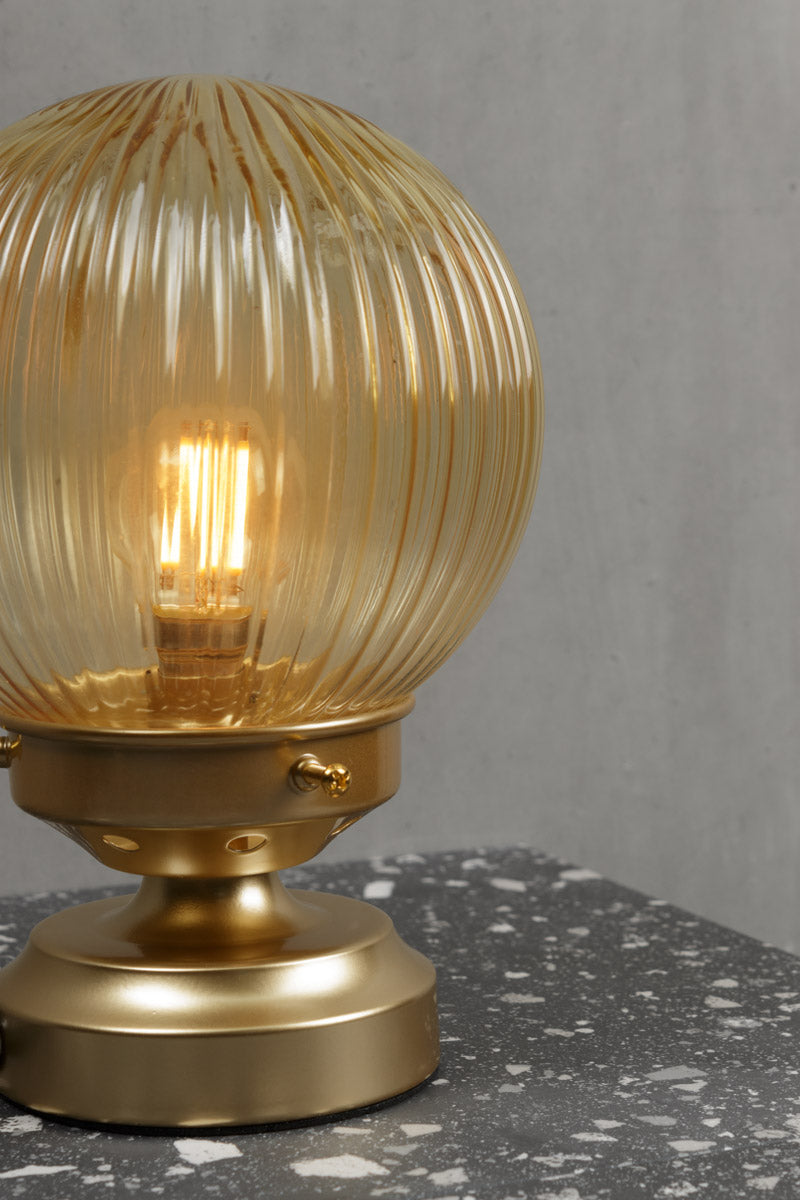 Close up of the Amber reeded glass ball lamp with a gold/brass base. 