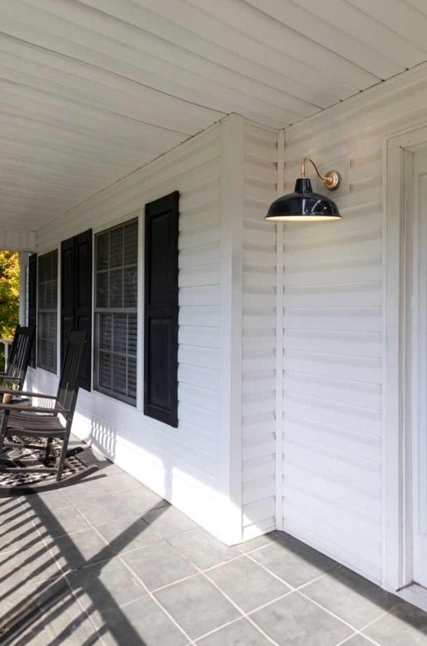 Polished brass wall sconce with black shade mounted on the front door porch