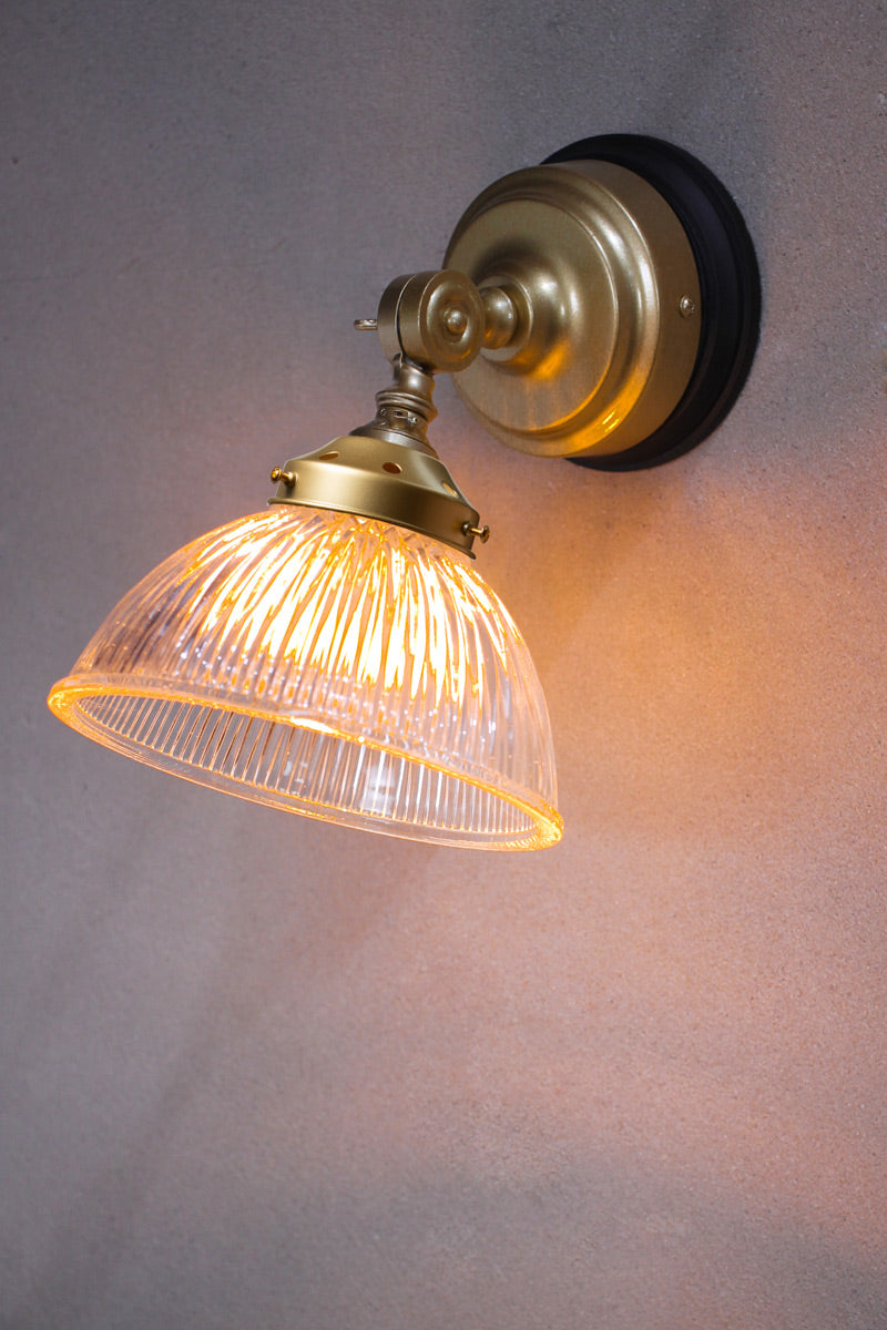 Gold/brass wall sconce with a ribbed glass sgade and black mounting block. 