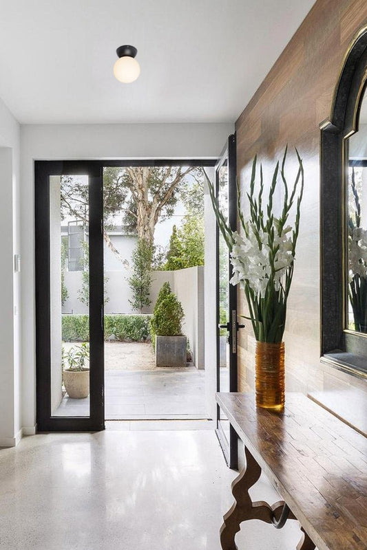 Black curved close to ceiling batten holder with opal glass ball shade in an entryway. 