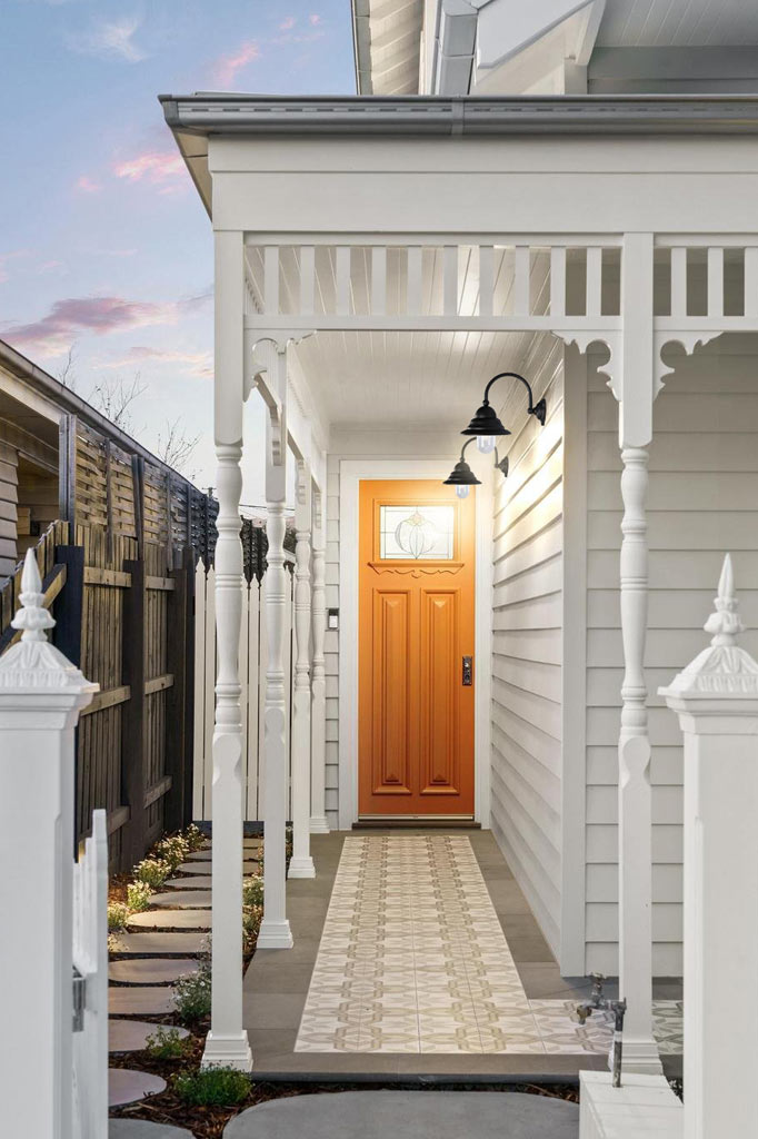 Two blaco gooseneck wall light on the bront porch of a white house with oragne door. 