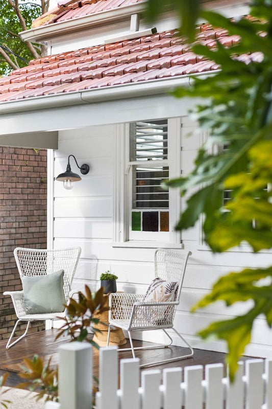 Black outdoor wall light with a gooseneck arm on a white, weather board house's porch. 