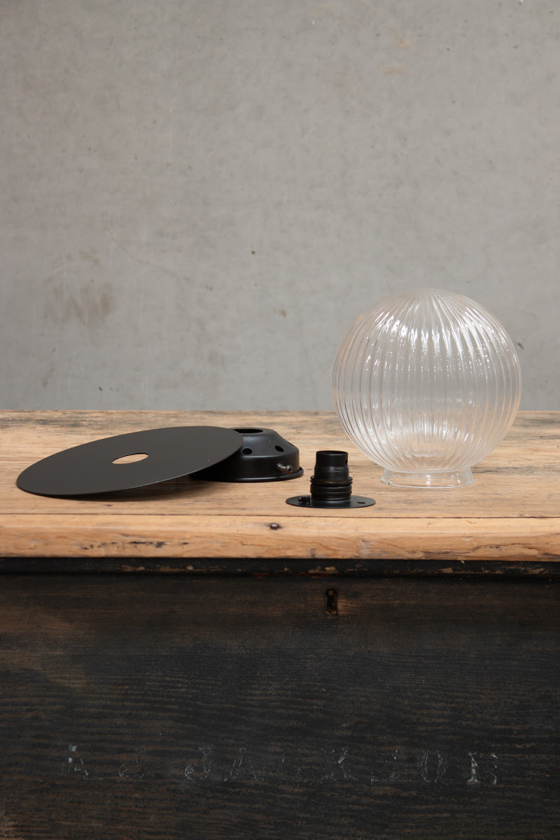 Dismantled image of a Small clear reeded glass ball shade n a small black brass disc. 