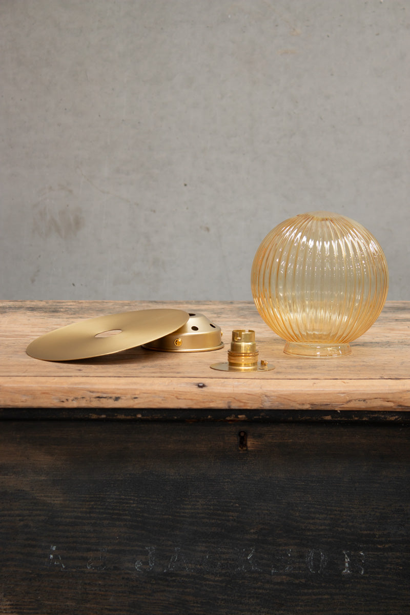 Dismantled image of a small amber reeded glass ball shade n a small brass disc. 