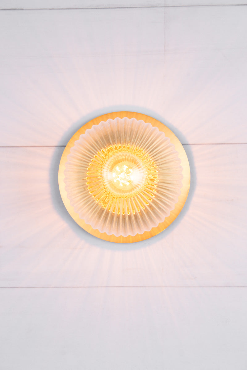 Front view of small clear reeded glass ball shade paired with a small brass disc. 