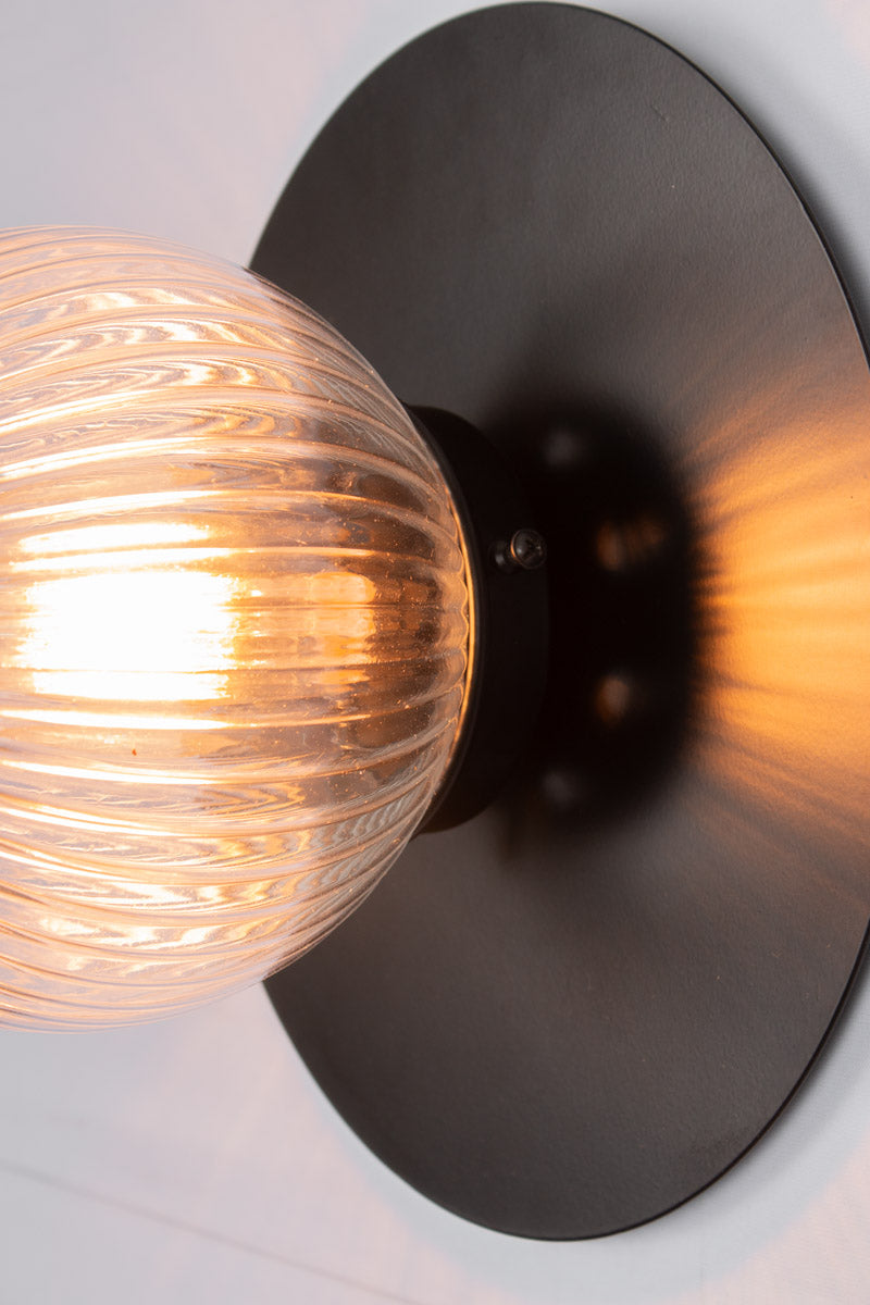 Close up of a small clear reeded glass ball shade n a large black brass disc.