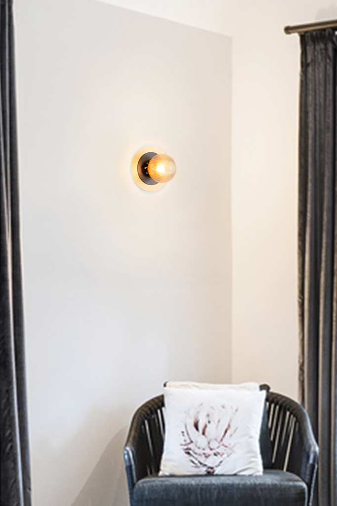 One amber reeded clear glass ball light with a small black disc and a large brass disc detail installed in a reading nook. 