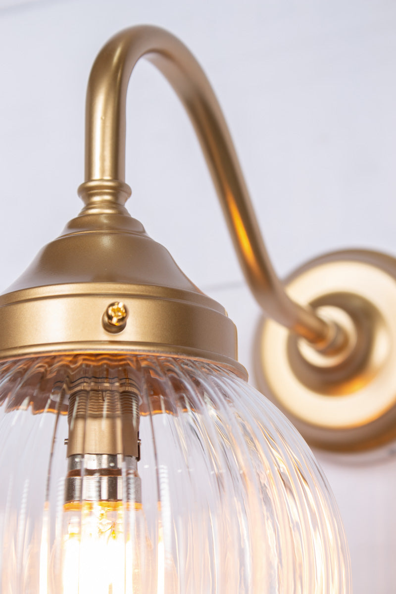 Exterior wall light with a gold/brass gooseneck arm and clear reeded shade, close up view.