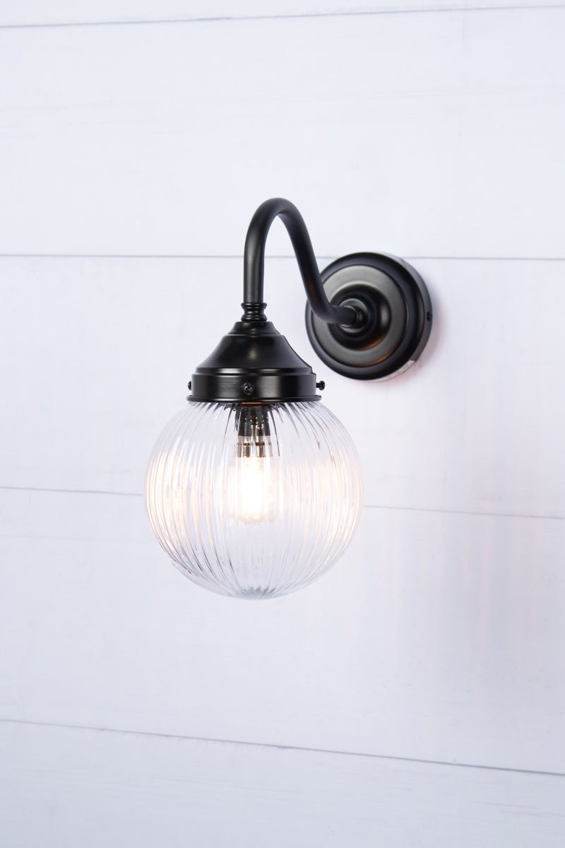 Exterior wall light with a clear gooseneck arm and clear reeded shade, side view.